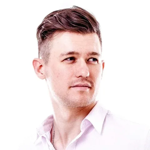Portrait of a man with styled hair wearing a light-colored collared shirt, looking to the side.