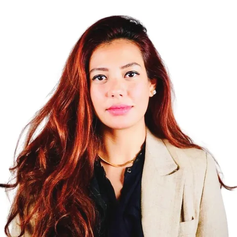 Portrait of a person with long auburn hair wearing a beige blazer, on a white background.