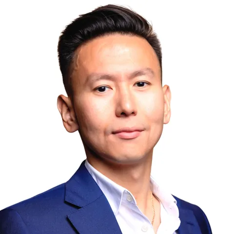 Portrait of a man with short dark hair wearing a navy suit jacket and white shirt, on a white background.