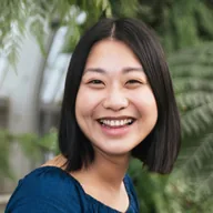 Smiling person posing in front of greenery.
